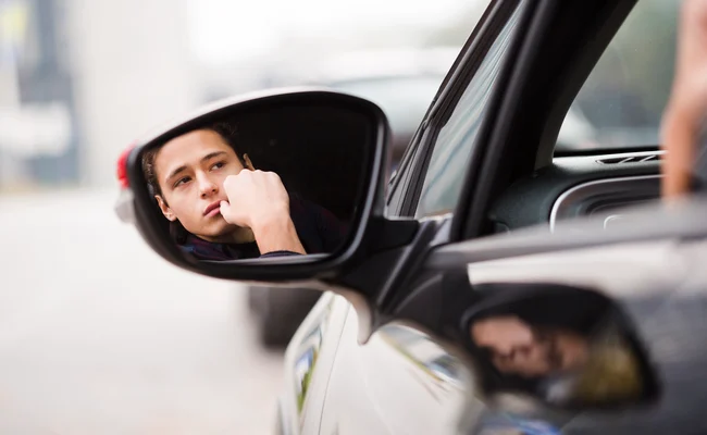 A quiet moment captured in a car’s side mirror, showing a man deep in thought, highlighting the emotional cost of neglecting key issues.