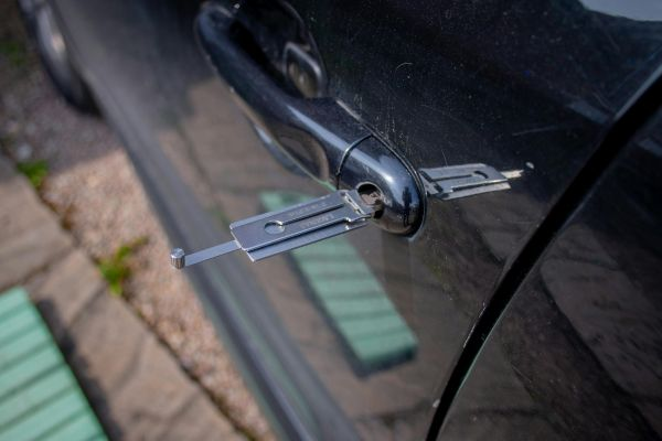 Car locksmith using tools to unlock a car door.
